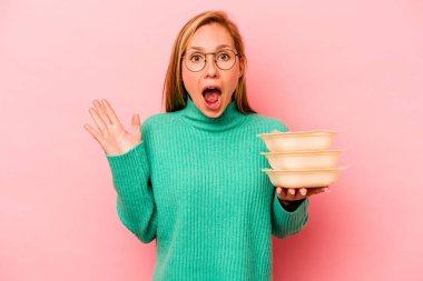 Beyaz tenli genç bir kadın pembe arka planda saklanmış vaziyette. Şaşırmış ve şok olmuş..