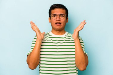 Latin kökenli genç bir adam mavi arka planda zaferi ya da başarıyı kutlarken şaşırmış ve şok olmuştu..