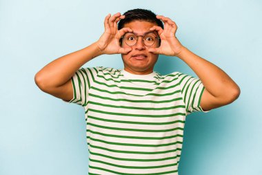 Genç İspanyol bir adam mavi arka planda izole edilmiş. Başarı fırsatı bulmak için gözlerini açık tutuyor..