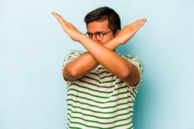 Genç İspanyol adam mavi arka planda izole edilmiş iki kolu çapraz tutuyor, inkar kavramı.