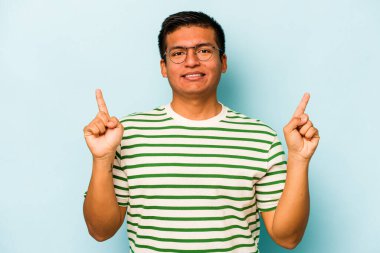 Mavi arka planda izole edilmiş genç İspanyol bir adam iki parmağı da boş bir alan gösteriyor..