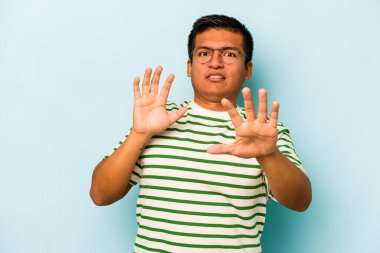 Genç İspanyol bir adam mavi arka planda izole edilmiş. Yakın bir tehlike nedeniyle şok oluyor.