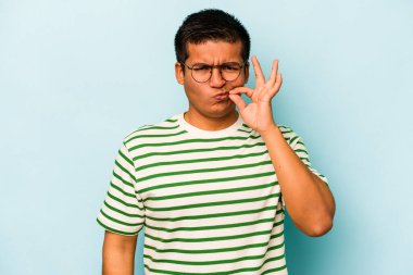 Genç İspanyol adam mavi arka planda izole edilmiş, parmakları dudaklarında bir sır saklıyor..