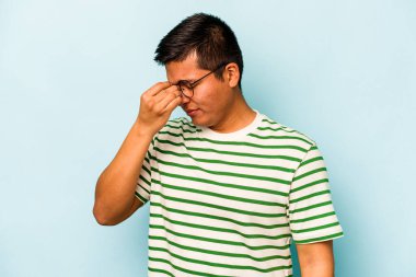 Genç İspanyol bir adam mavi arka planda izole edilmiş, başı ağrıyor, yüzüne dokunuyor..