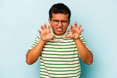 Mavi arka planda izole edilmiş genç İspanyol bir adam pençelerini bir kediyi taklit ederken gösteriyor, agresif bir hareket..