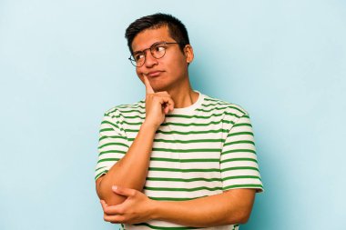 Latin kökenli genç bir adam mavi arka planda izole edilmiş. Bir strateji planlıyor, bir iş yolu düşünüyor..