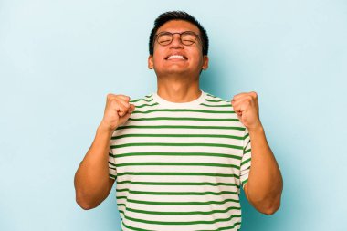 Mavi arka planda izole edilmiş genç İspanyol bir adam zaferi, tutkuyu ve coşkuyu kutluyor, mutlu bir ifade..