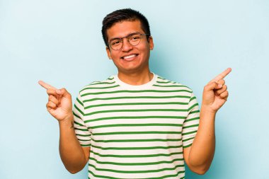 Mavi arka planda izole edilmiş genç İspanyol adam farklı kopya alanlarını gösteriyor, birini seçiyor, parmaklarıyla gösteriyor..