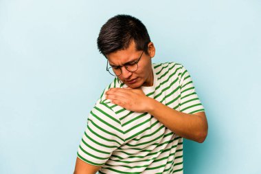 Mavi arka planda izole edilmiş genç İspanyol bir adam omuz ağrısı çekiyor..