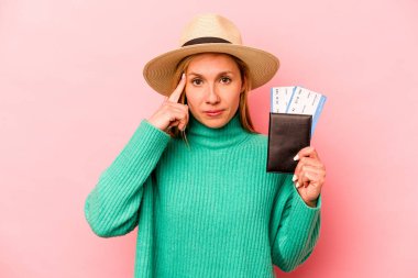 Pasaportu olan beyaz bir kadın pembe arka planda izole edilmiş bir şekilde tapınağı işaret ediyor, düşünüyor ve bir göreve odaklanıyor..