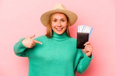 Pasaportu olan beyaz bir kadın pembe arka planda izole edilmiş, gömlekli bir fotokopiciyi işaret ediyor, gururlu ve kendinden emin.