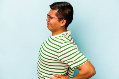 Genç İspanyol bir adam mavi arka planda izole edilmiş sırt ağrısı çekiyor..