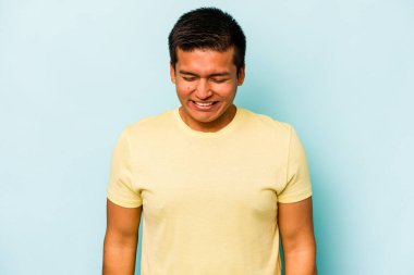 Mavi arka planda izole olmuş genç İspanyol adam gülüyor ve gözlerini kapıyor, rahatlamış ve mutlu hissediyor..