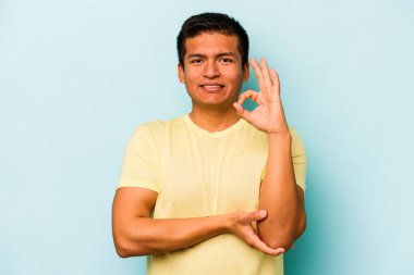 Mavi arka planda izole edilmiş genç İspanyol bir adam bir göz kırptı ve elleriyle iyi bir jest yaptı..