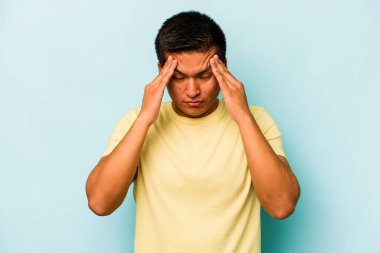 Genç İspanyol adam mavi arka planda izole edilmiş tapınaklara dokunuyor ve baş ağrısı çekiyor..