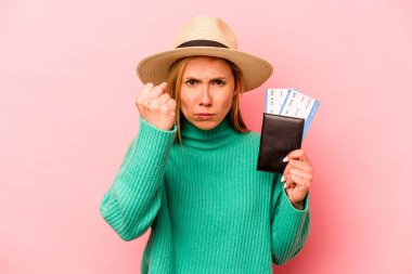 Pasaportu olan beyaz bir kadın pembe arka planda izole edilmiş. Kameraya yumruk, agresif yüz ifadesi gösteriyor..
