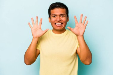 Genç İspanyol bir adam mavi arka planda izole edilmiş. Hoş bir sürpriz bekliyor. Heyecanlı ve el kaldırıyor..
