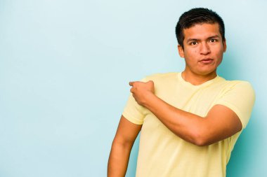 Mavi arka planda izole edilmiş genç İspanyol adam gülümsüyor ve boş alanda bir şeyler gösteriyor..