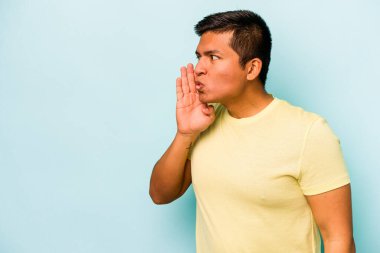 Mavi arka planda izole edilmiş genç İspanyol bir adam gizli bir sıcak fren haberi veriyor ve yana bakıyor.