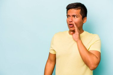 Genç İspanyol bir adam mavi arka planda izole edilmiş. Gördüğü bir şey yüzünden şok oluyor..