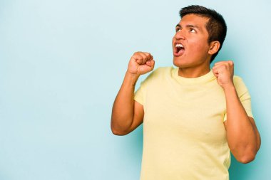 Mavi arka planda izole edilmiş genç İspanyol bir adam zaferden sonra yumruk kaldırıyor, kazanan konsept..