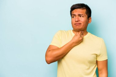 Genç İspanyol bir adam mavi arka planda izole edilmiş kafasının arkasına dokunuyor, düşünüyor ve bir seçim yapıyor..