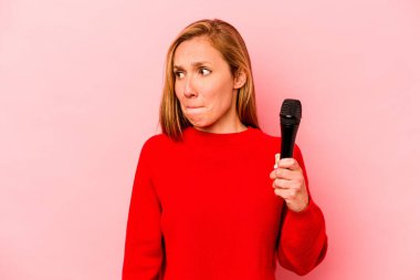 Pembe arka planda izole edilmiş genç beyaz kadın kafası karışmış, şüpheli ve güvensiz hissediyor..