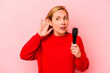 Pembe arka planda izole edilmiş genç beyaz kadın bir dedikoduyu dinlemeye çalışıyor..