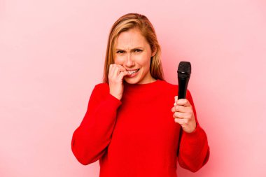 Pembe arka planda izole edilmiş, tırnak yiyen, gergin ve endişeli genç beyaz bir kadın..