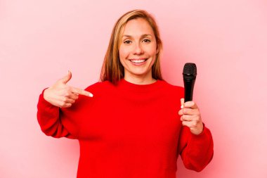 Pembe arka planda izole edilmiş genç beyaz kadın gömlek fotokopisini elle gösteriyor, gururlu ve kendinden emin.