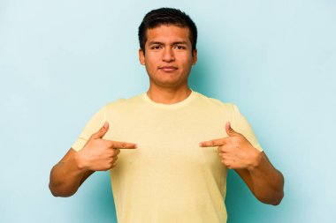 Genç İspanyol bir adam mavi arka planda izole edilmiş. Parmakları aşağıda, olumlu hisler içinde..