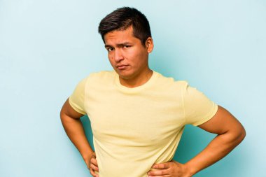 Mavi arka planda izole edilmiş, hoşnutsuzca kaşlarını çatmış, kollarını kavuşturmuş genç bir İspanyol..