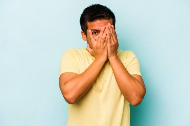 Genç İspanyol adam mavi arka planda izole edilmiş. Korkmuş ve gergin parmaklarıyla göz kırp..