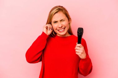 Kafkasyalı genç şarkıcı kadın pembe arka planda izole edilmiş kulakları elleriyle kapatıyor..