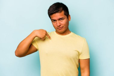 Mavi arka planda izole edilmiş genç bir İspanyol gömlek fotokopisini elle işaret ediyor, gururlu ve kendinden emin.