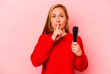 Pembe arka planda izole edilmiş genç beyaz kadın ya sır saklıyor ya da sessizlik istiyor..