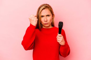 Pembe arka planda izole edilmiş genç beyaz kadın kameraya yumruğunu, agresif yüz ifadesini gösteriyor..