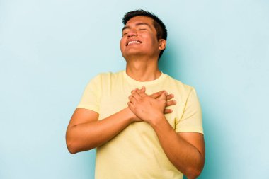 Mavi arka planda izole edilmiş genç İspanyol adam, avuçlarını göğsüne bastıran dostça bir ifadeye sahiptir. Aşk konsepti.