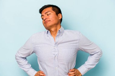 Genç İspanyol adam mavi arka planda izole edilmiş. Amaçlarına ve amaçlarına ulaşmayı hayal ediyor.