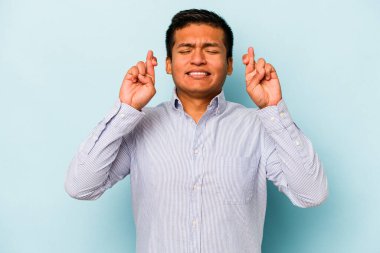 Genç İspanyol adam mavi arka planda izole edilmiş şans dilemek için şans diliyor.