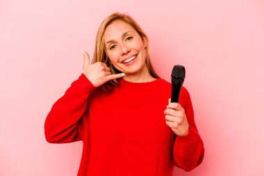 Pembe arka planda izole edilmiş genç beyaz kadın parmaklarıyla bir cep telefonu hareketi gösteriyor..