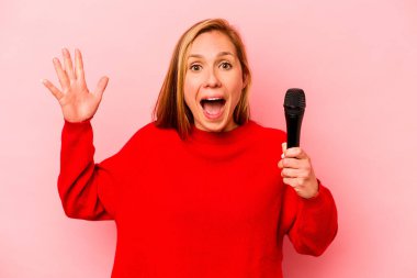 Pembe arka planda izole edilmiş genç beyaz kadın hoş bir sürpriz alıyor, heyecanlı ve el kaldırıyor..