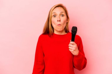 Pembe arka planda izole edilmiş genç beyaz kadın omuzlarını silker ve gözleri açık kalır..