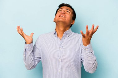 Genç İspanyol adam mavi arka planda izole edilmiş gökyüzüne haykırıyor, yukarı bakıyor, hayal kırıklığına uğramış..