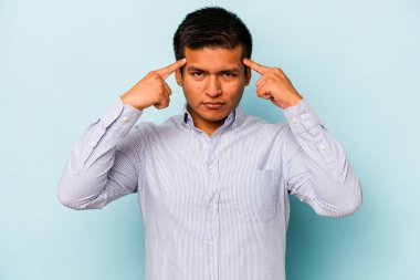 Mavi arka planda izole edilmiş genç İspanyol bir adam bir göreve odaklanmış, işaret parmaklarını işaret ediyor..