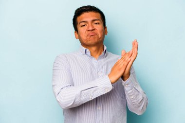 Genç İspanyol adam mavi arka planda izole edilmiş enerjik ve rahat hissediyor, ellerini ovuşturuyor kendinden emin..