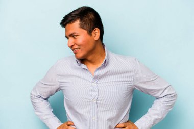 Latin kökenli genç adam mavi arka planda izole edilmiş. Kendine güveniyor. Kalçaları tutuyor..