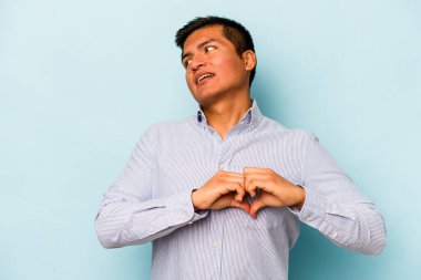Mavi arka planda izole edilmiş genç İspanyol adam gülümsüyor ve elleriyle kalp şeklini gösteriyor..