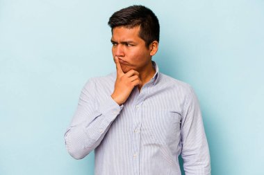 Mavi arka planda izole edilmiş genç İspanyol bir adam ya sır saklıyor ya da sessizlik istiyor..