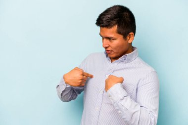 Mavi arka planda izole edilmiş genç İspanyol adam parmağını göstererek şaşırdı, geniş bir gülümsemeyle..